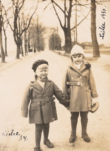 Dzieci ok. 6 lat, stoją obok siebie na alei parkowej, w tle bezlistne drzewa.