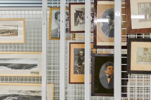 Magazyn muzeum. Na kratach wiszą zdjęcia w drewnianych oprawach. 