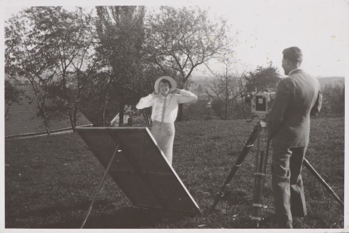 Młoda kobieta pozująca w parku pałacowym do fotografii, mężczyzna przy dużym aparacie fotograficznym na statywie.