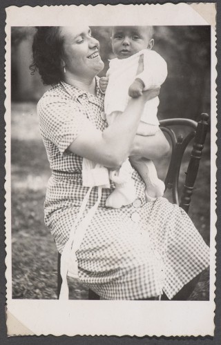 Uśmiechnięta kobieta w sukience w kratkę trzyma roczne dziecko.