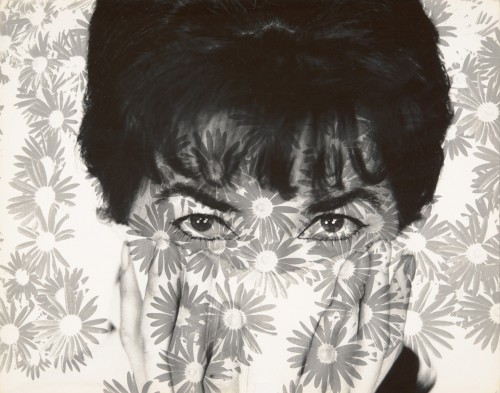 Portret młodej dziewczyny widocznej poprzez tkaninę zadrukowaną w cieniowane, szare kwiaty. 