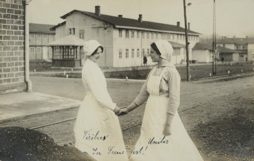 Dwie kobiety podające sobie ręce, ubrane w faruchy pielęgniarskie.